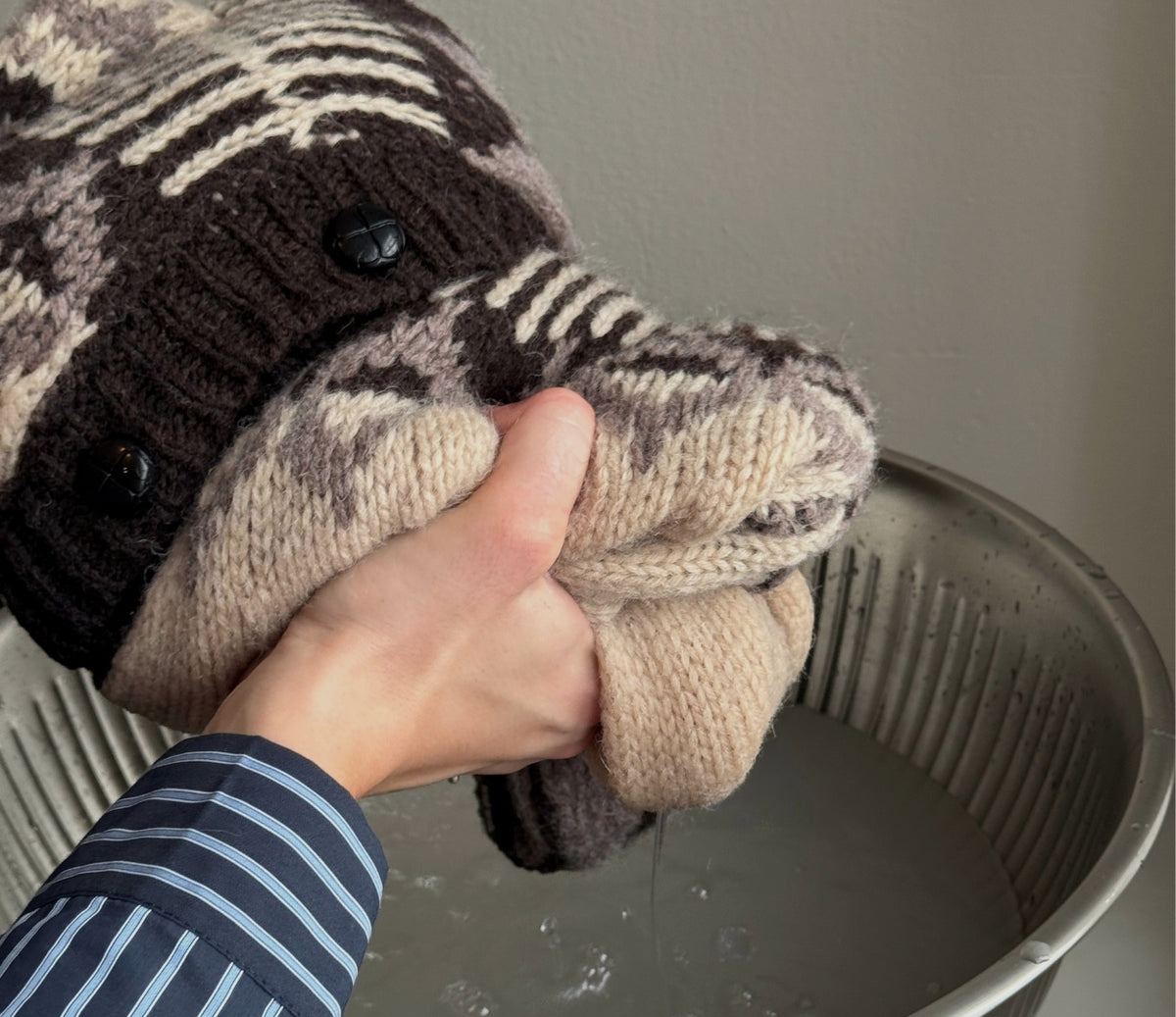 Image of a knit sweater being lifted out of the water while the excess water is gently squeezed out.