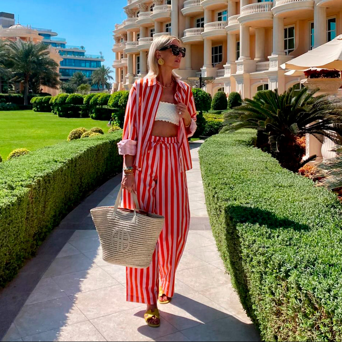 Woman wearing a red and white striped matching set from Lollys Laundry with a shirt and trousers, styled with a white top, sunglasses and a woven bag.