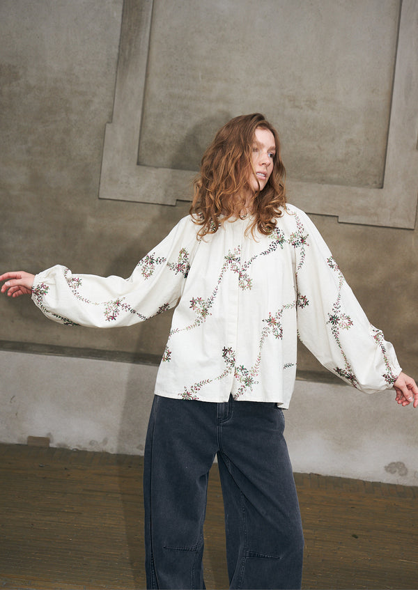 Woman wearing a cream blouse with embroidered floral motifs and dark denim jeans from Lollys Laundry.