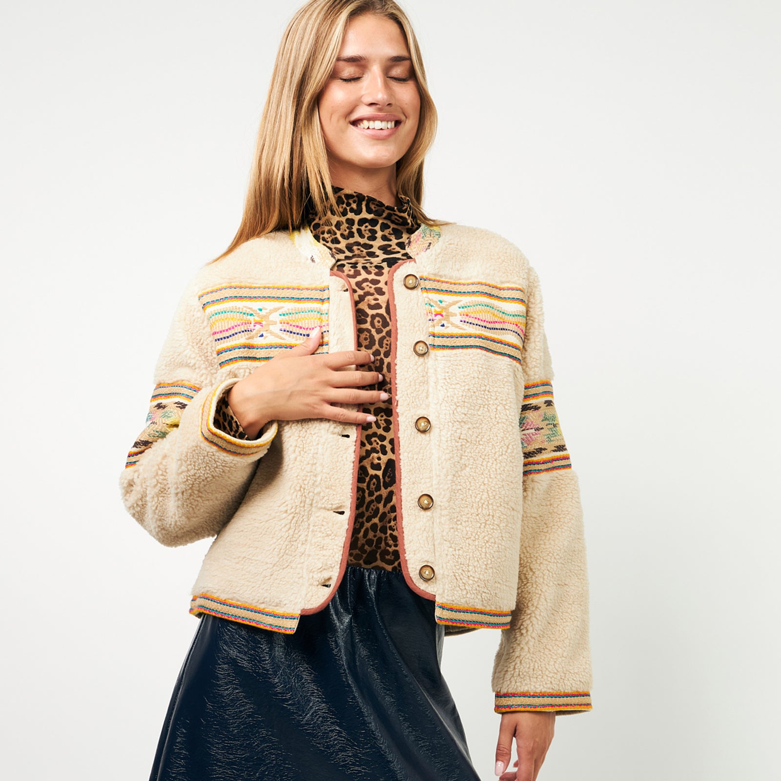Model wearing a beige jacket with colourful embroidery and buttons from Lollys Laundry, styled with a leopard turtleneck top and a dark blue skirt.