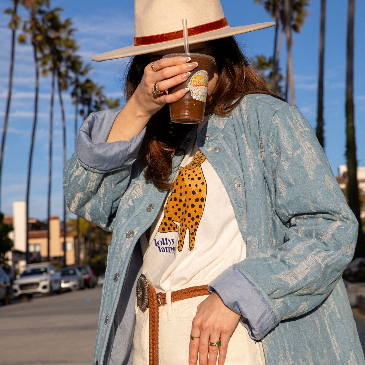 Woman wearing a light blue patterned jacket, styled with a white leopard print T-shirt, light trousers and a beige hat.