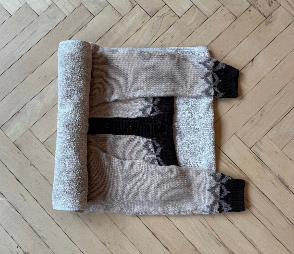 Image showing the knit sweater lying flat on a towel, which is being rolled up to absorb some of the excess water from the sweater.