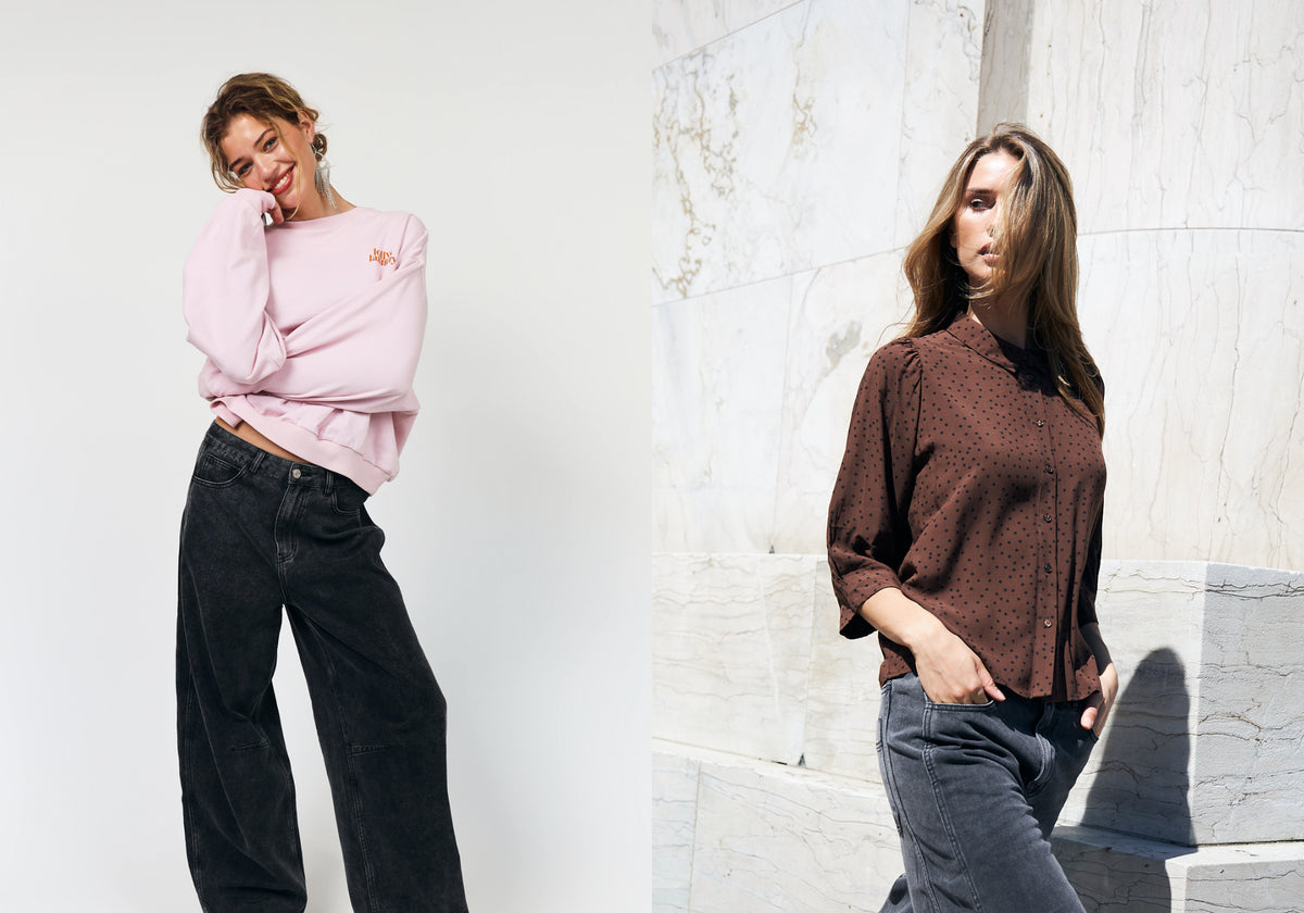 Two women in casual outfits. One wears a light pink sweatshirt with dark grey jeans, while the other wears a brown shirt with small black polka dots and grey jeans.