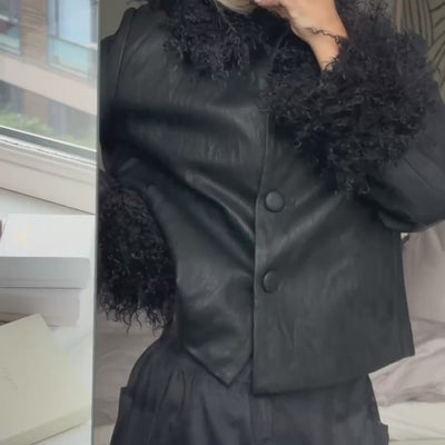 Video featuring a woman wearing a black jacket with curly fur-look trim at the collar and cuffs, styled with dark checked trousers.